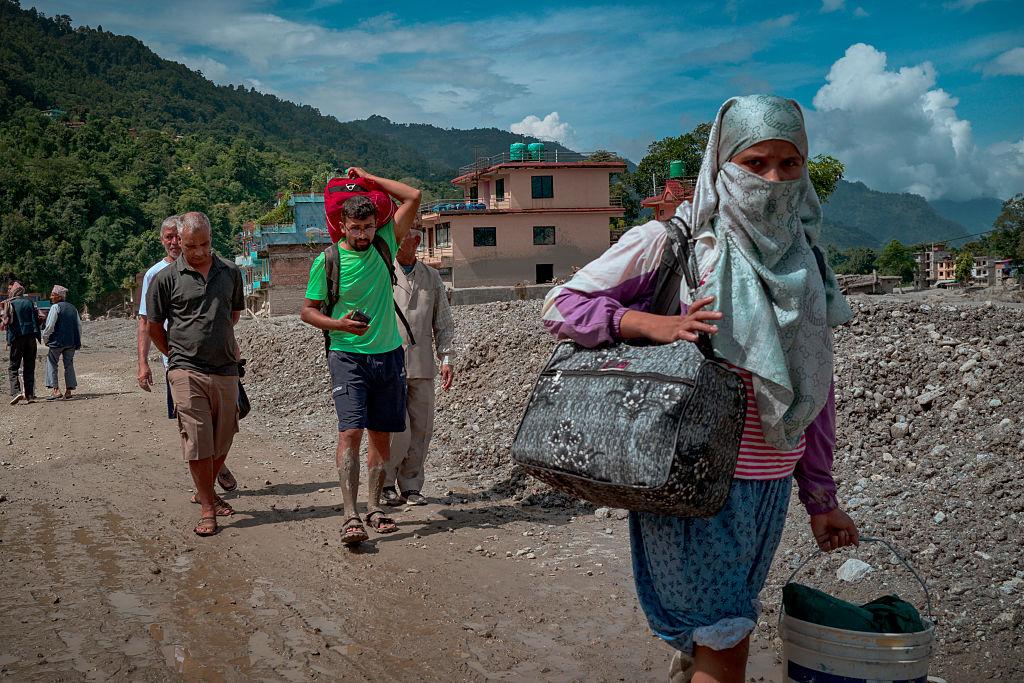 Displaced residents carrying their belongings along a muddy, debris-strewn track in flood-hit Nepal