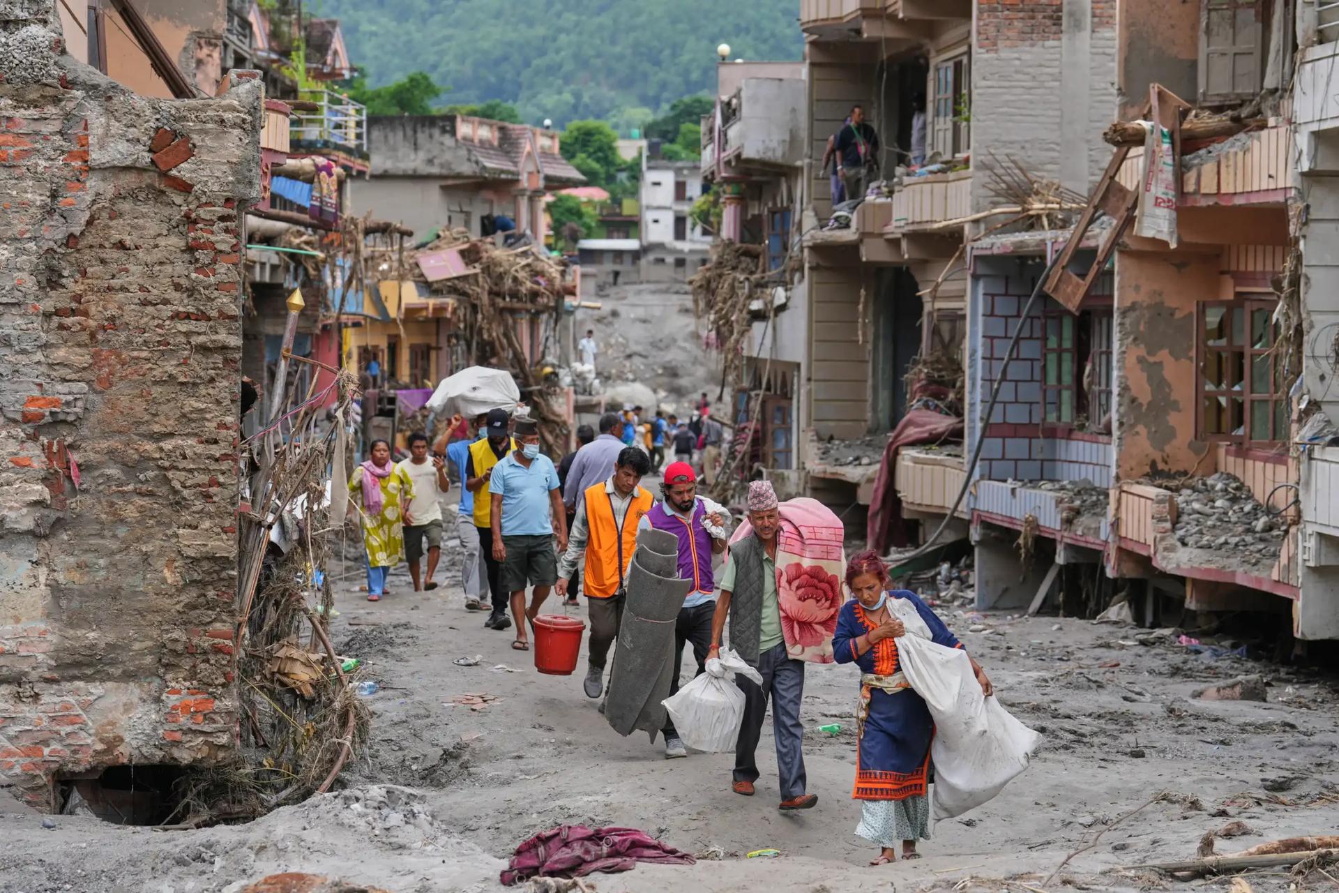 Residents carrying salvaged belongings through a flood-damaged street in Nepal