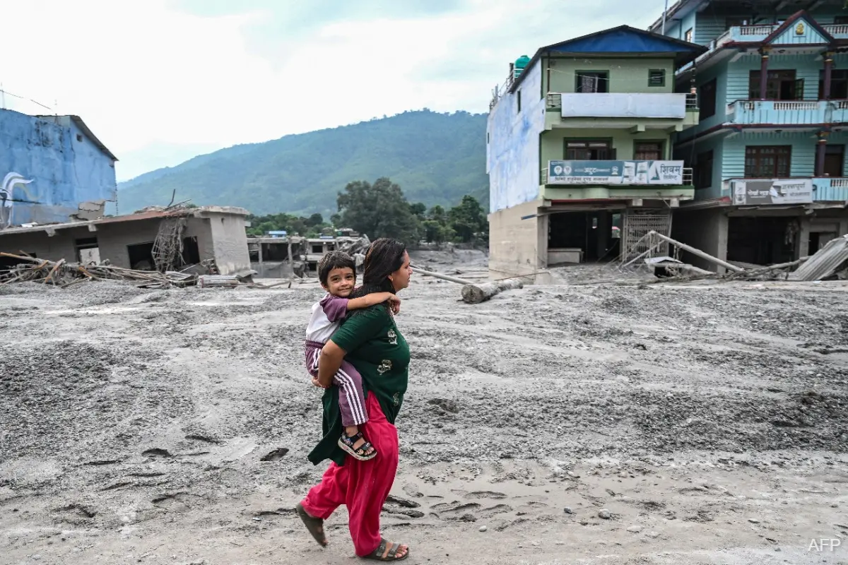 A mother carrying her child through a mud-covered, flood-damaged neighborhood in Nepal